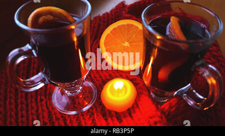 Glühwein im Glas Becher, brennende Kerze auf einem dunklen roten Hintergrund. Red Hot Wein Stockfoto