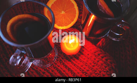 Glühwein im Glas Becher, brennende Kerze auf einem dunklen roten Hintergrund. Red Hot Wein Stockfoto