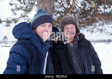 Zwei reife Männer, Vater und Sohn, gekleidet in warme Kleidung sniling und Kamera beim Walking outdoor im Winter Tag Stockfoto