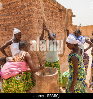 Afrikanische Frauen quetschen Getreide mit traditionellen Holzmöbeln Mörser und Stößel, Ouagadougou, Burkina Faso. Stockfoto