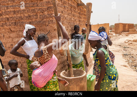 Afrikanische Frauen quetschen Getreide mit traditionellen Holzmöbeln Mörser und Stößel, Ouagadougou, Burkina Faso. Stockfoto