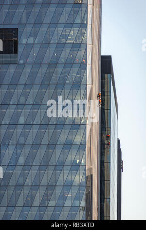 Zwei Fensterputzer auf der Seite von einem Wolkenkratzer tragen orange Fangvorrichtung ausgesetzt Stockfoto