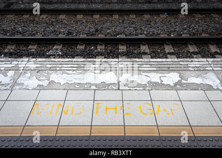 Eine verblasste und abgenutzt "Mind the Gap"-Zeichen auf der Plattform von einem Bahnhof mit dem Zug schienen im Hintergrund Stockfoto