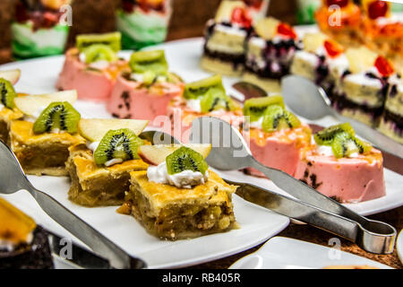 Close up viel leckeres Dessert Gebäck Kuchen Törtchen in einer Reihe. Frisch, bunt, bunt, Grün, Gelb, Weiß und Pink sweet berry Desserts, werden Stockfoto