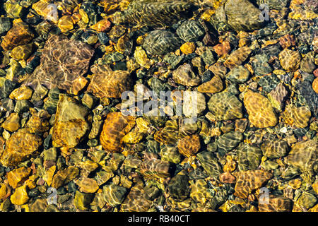 Bunte rolling stones Muster mit immer noch Wasser. Bunte meer Steine unter Wasser. Irisierende das Sonnenlicht auf die Steine. Transparente klare Wasser des Stockfoto