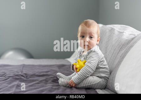 Sitzung Baby auf grauem Teppich mit gelben Ball Spielzeug. Mutterschaft und neues Leben Konzept Stockfoto