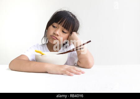 Portrait von asiatischen Kind Mädchen weigern, Lebensmittel oder gelangweilt, Kind, Anorexie und weiße Holztisch mit weißem Hintergrund zu essen. Stockfoto