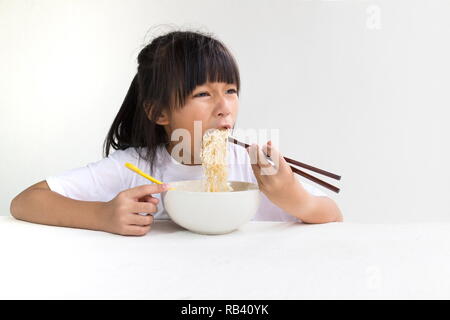 Portrait von asiatischen Kind Mädchen essen Instant Nudelsuppe mit weißen Holzmöbeln und weißen Hintergrund. Stockfoto