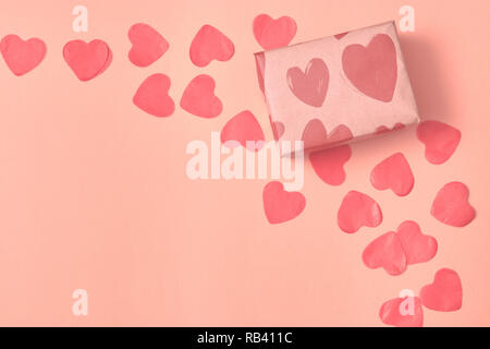 Geschenk in Kraftpapier mit roten Herzen auf rosa Hintergrund mit Herzen. Das Konzept der Valentinstag. Blick von oben. kopieren. Stockfoto