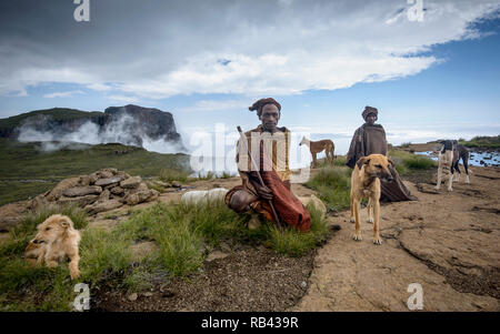 Zwei afrikanische Männer in ihre traditionelle Basotho decken und Kopfbedeckungen gewickelt, hockte auf dem Berg oben mit ihren vier Hunden. Full Color Image Stockfoto
