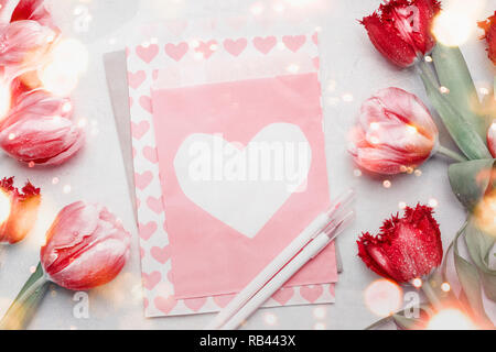 Rote Tulpen um Papier mit Herz auf dem Desktop Hintergrund mit Markierungen, Ansicht von oben. Kreative festliche selbstgemachten Grußkarten zum Valentinstag, Mutter Stockfoto