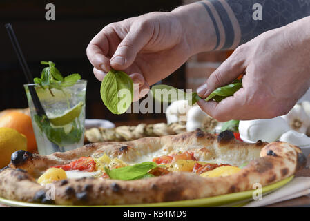 Dressing Pizza nach dem Backen, treibt's frisches Basilikum mit Händen Stockfoto