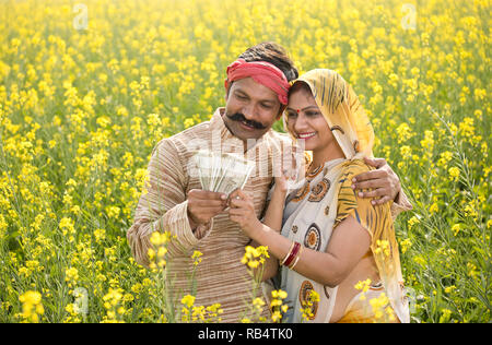 Happy indischen Bauern mit Frau holding Indian Rupee Notizen in der Landwirtschaft Feld Stockfoto