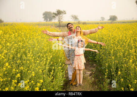 Ländlichen indischen Familie, die mit der Waffe in der Raps landwirtschaftliches Feld ausgestreckten Stockfoto