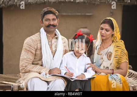 Ländlichen indischen Eltern mit Tochter tun Schule Hausaufgaben im Village Stockfoto