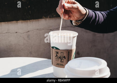 Prag, Tschechische Republik - 26. August 2018: weibliche Hand rühren Kaffee von Starbucks in White Paper Cup auf einem Tisch im Freien im Sommer. Starbucks i Stockfoto