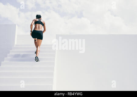 Rückansicht eines weiblichen Athleten laufen die Treppe eines Gebäudes. Frau in fitness Verschleiß tun Workout auf Treppen. Stockfoto