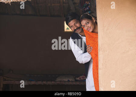 Portrait von Happy indischen Ehepaar in traditioneller Kleidung peeking aus Haus im Dorf Stockfoto