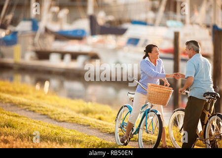 Paar mittleren Alters halten Sie Hände und an jeder anderen schauen beim Fahrrad fahren auf einer Yacht Marina. Stockfoto