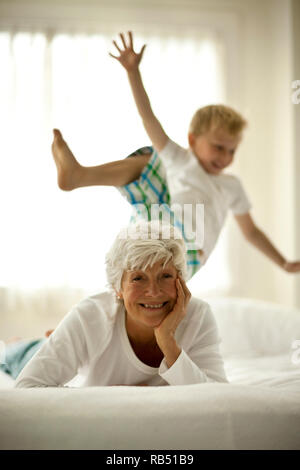 Gerne ältere Frau liegt auf dem Bett mit ihrem Enkel , im Hintergrund. Stockfoto