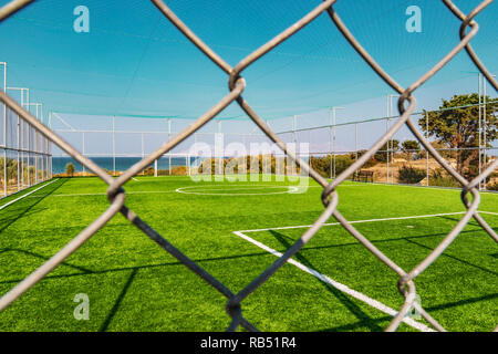 Blick auf einen grünen Fußballplatz hinter einem Metallzaun, in der Nähe des Meeres. Stockfoto