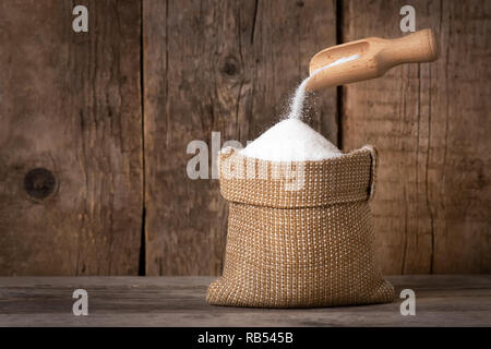 Weißzucker in sackleinen Tasche und Schaufel auf Holz- Hintergrund Stockfoto