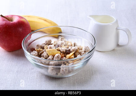 Gesund essen mit Corn Flakes Müsli in eine Schüssel geben, Apfel, Banane und Glas mit Milch. Frühstück am Morgen. Stockfoto