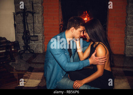 Zart und romantisch Bild der jungen Paare zusammen am Kamin sitzen. Sie berühren sich ihre Stirn und Blick in die Augen. Kerl halten Sie die Hand auf den Unterarm. Stockfoto