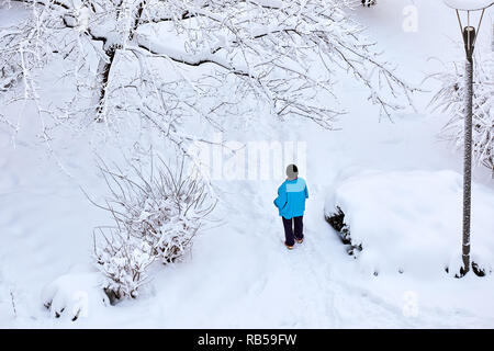 Frau trägt ein blaues Fell und schwarzen Weal steht in einem Park bedeckt mit Schnee im Winter. Blick von oben. Stockfoto