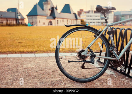 Sattel und Hinterrad Detail einer Vintage Fahrrad auf einem Boden Straße gegen blurry wiese feld und historischen Gebäude Hintergrund geparkt Stockfoto