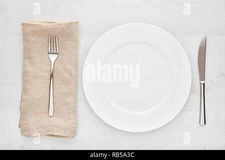 Leere weiße runde Keramik Teller, Gabel, Messer und Serviette auf weiße Holztisch. Von oben nach unten anzeigen. Stockfoto