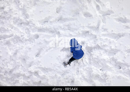Antenne oben Blick auf einen Blick zurück kleiner Junge mit Blue Coat Spielen im Schnee Stockfoto