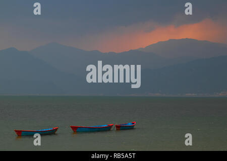 Bunte Boote in See in Pokhara in Nepal bei einem Sonnenuntergang in einem Regensturm Himmel plötzlich öffnen und Malerei die Berge im Hintergrund mit Licht Stockfoto