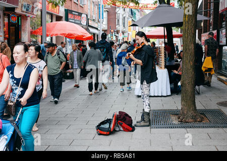 Junge asiatische Frau Straßenmusiker spielen Geige und versuchen, Geld von Passanten in Chinatown, Montreal, Kanada zu sammeln. Stockfoto