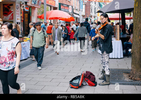 Junge asiatische Frau Straßenmusiker spielen Geige und versuchen, Geld von Passanten in Chinatown, Montreal, Kanada zu sammeln. Stockfoto