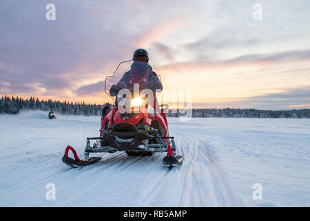 Person, die einen Snowmobile bei Sonnenaufgang über einen zugefrorenen See im Norden Schwedens. Während eine Sunset Tour in der Nähe der Ice Hotel. Gefrorenen See geöffnet. Stockfoto