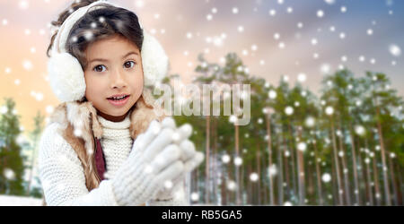 Kleines Mädchen Ohrenschützer tragen über Winter Forest Stockfoto