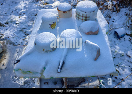 Gefrorene Alten rostigen Metall Aufläufe auf einem Tisch unter dem Schnee im Winter. Wie ein Nach dem Krieg oder wie ein Postapocalypse anzeigen. Stockfoto
