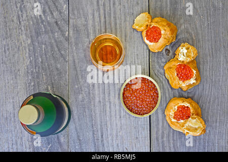 Eclairs mit rotem Kaviar, Kaviar in der Dose, eine Flasche und ein Glas Cognac in einem rustikalen vintage Hintergrund. Stockfoto