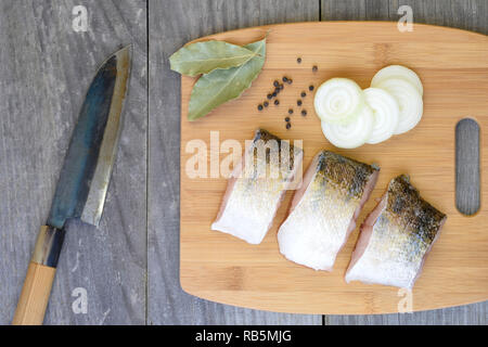 Stücke von Fisch auf einem Schneidebrett mit Gewürzen auf Holz rustikale vintage Hintergrund mit einem Küchenmesser. Stockfoto