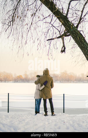 Thema Liebe und aktive Erholung auf rustikalen Charakter. Junges Paar kaukasischen Kerl und ein Mädchen stehen wieder im vollen Wachstum Hand in Hand im Winter auf Schnee pier overlo Stockfoto