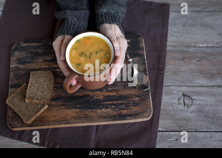 Frau Hände halten Tasse Gemüsesuppe auf Holzuntergrund - gesunde Winter vegetarisches Essen, gemütliche wärmende Suppe. Stockfoto