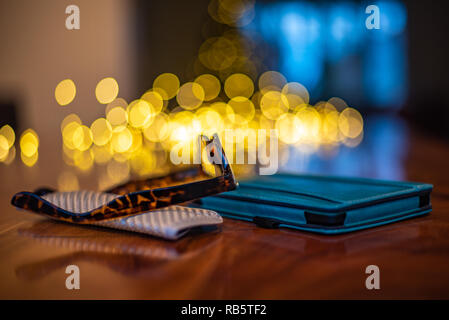 Lesebrillen und e-Reader die Verlegung in eine Walnuss Tisch mit Lichterketten auf dem Hintergrund. Stockfoto