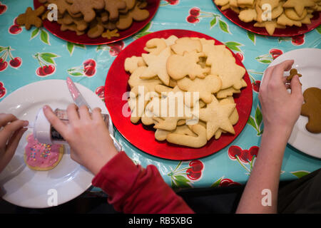 Auf einem Tisch mit Diners Hände in den Prozess der Dekoration frisch gebackene Kekse für Weihnachten Weihnachten themed Stockfoto