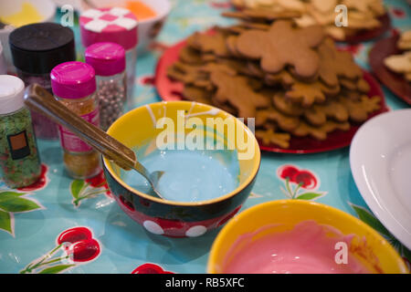 Blick nach unten auf einen Tisch voller Zutaten cookies mit Schalen von farbigen Glasur und verschiedene zuckerhaltige Elemente für Weihnachten zu dekorieren Stockfoto