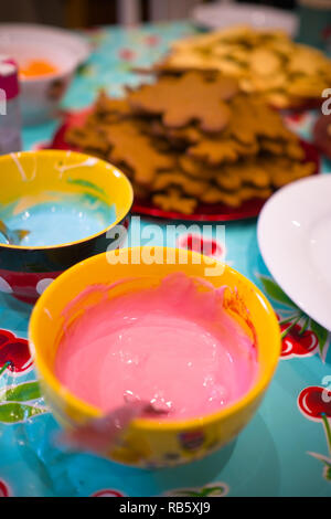 Blick nach unten auf einen Tisch mit Schüsseln der Vereisung Zutaten Stapel Cookies auf Platten im Hintergrund zu verzieren Stockfoto