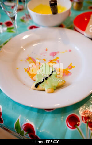 Die Hälfte dekoriert hausgemachte Plätzchen geformt wie ein Weihnachtsbaum, bedeckt mit grünen Vereisung und Lügen in Vereisung von anderen Bemühungen auf eine weisse Platte Stockfoto