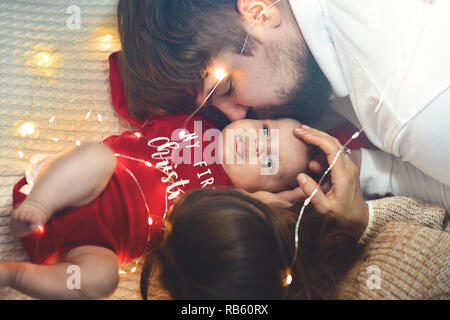 Ansicht von oben. Mutter und Vater küsst Baby im Bett. Dem kleinen neugeborenen Kind in weißen Bett. Elternschaft Konzepte. Liebe und Glück. Die Pflege des neuen Lebens. Stockfoto