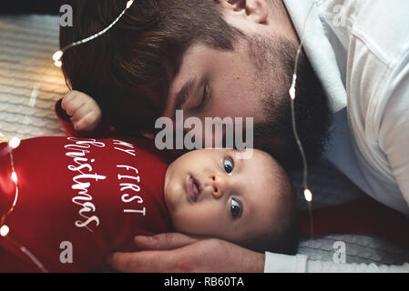 Ein junger Vater küsst seine neugeborene Tochter. Vater und neugeborenes Baby Nahaufnahme. Vater und Kind auf dem Bett liegen. Stockfoto