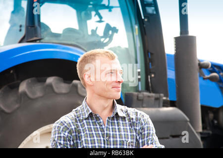 Junger attraktiver Mann in der Nähe von einem Traktor. Konzept der Landwirtschaft und Feld arbeitet. Stockfoto